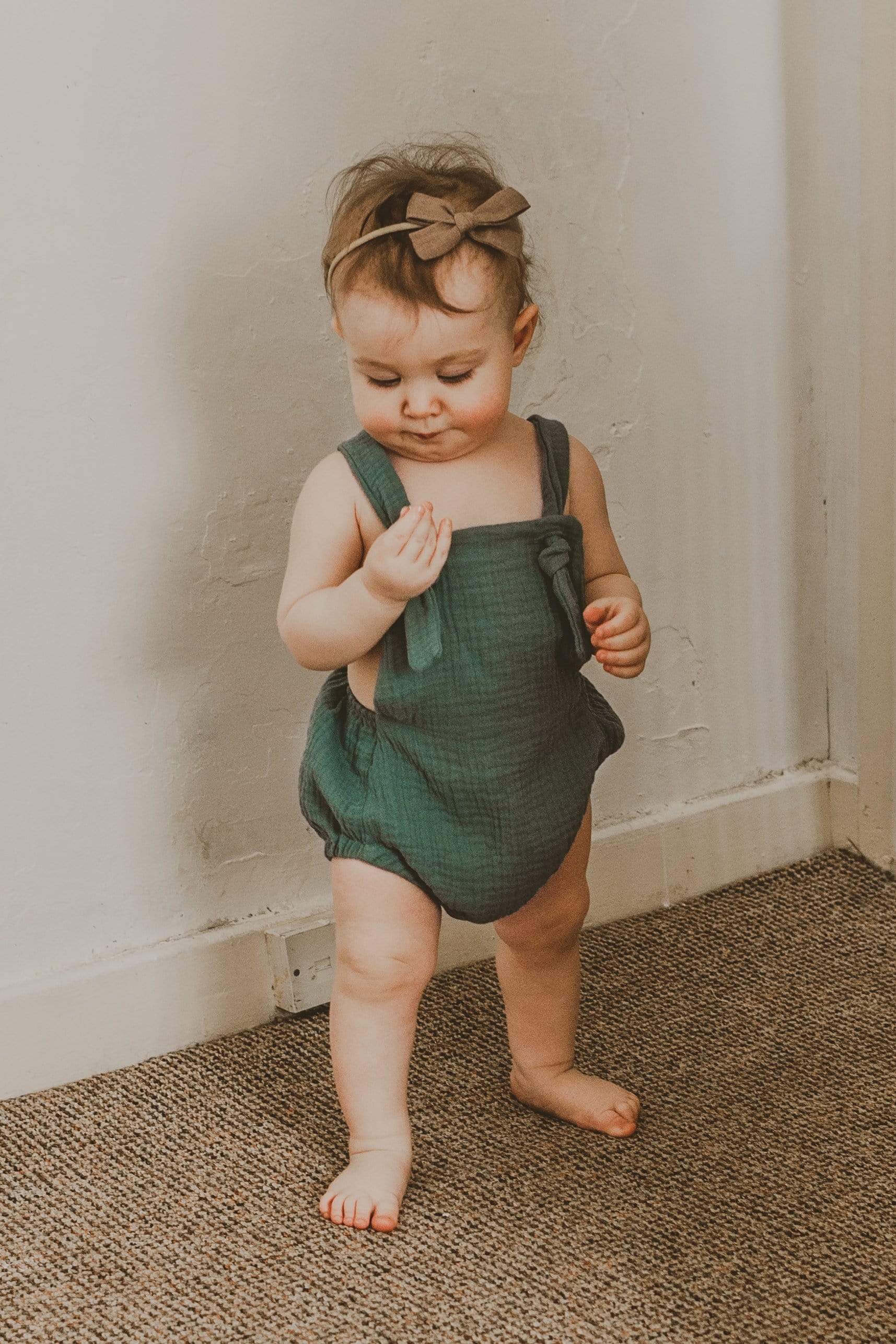 girl walking into a room wearing the forest green bohemian handmade summer romper with adjustable straps easy to layer up hippy sustainable baby toddler clothing 