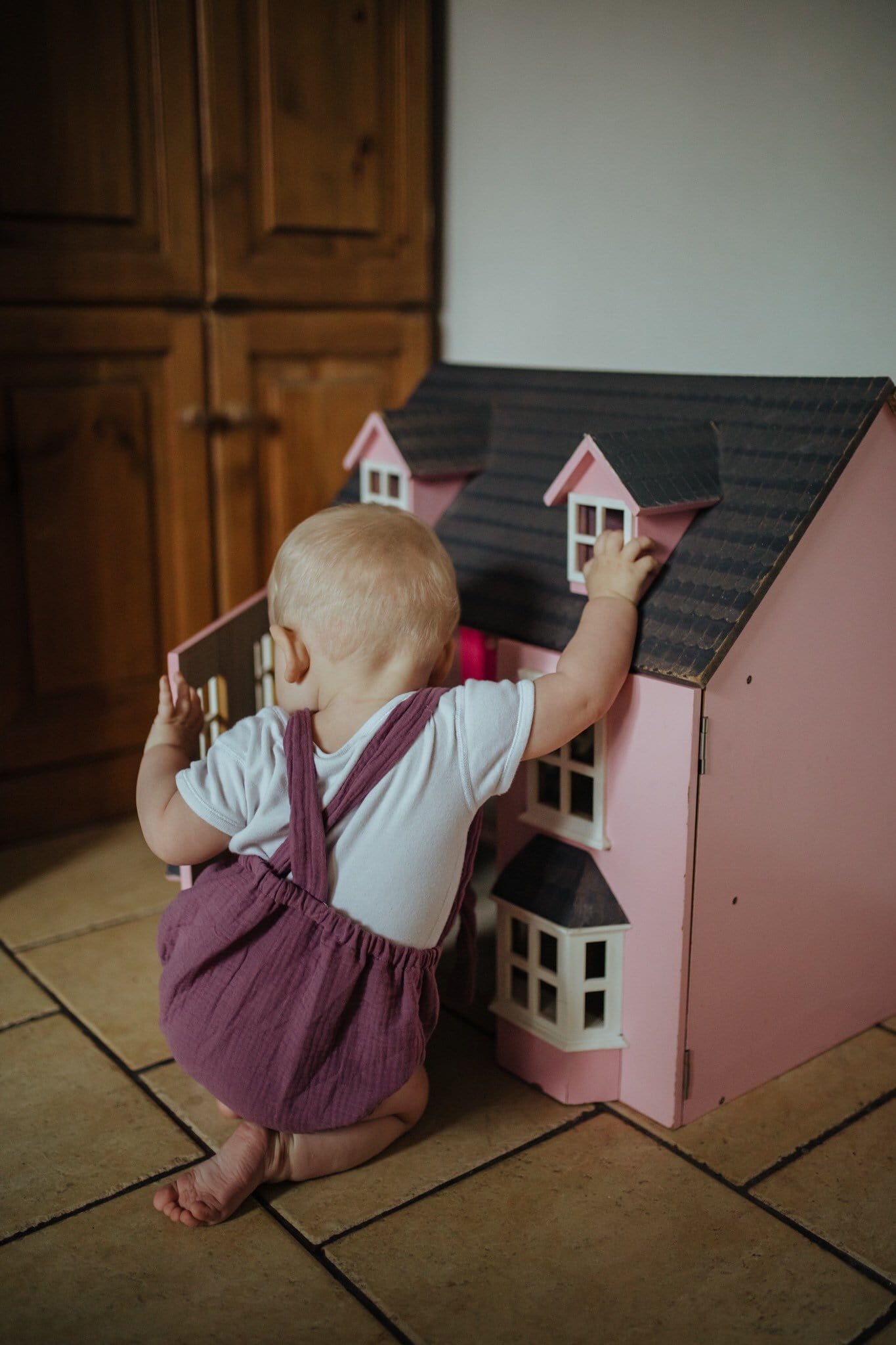 girl playing with dolls house wearing the purple bohemian handmade summer romper with adjustable straps easy to layer up hippy sustainable baby toddler clothing unisex