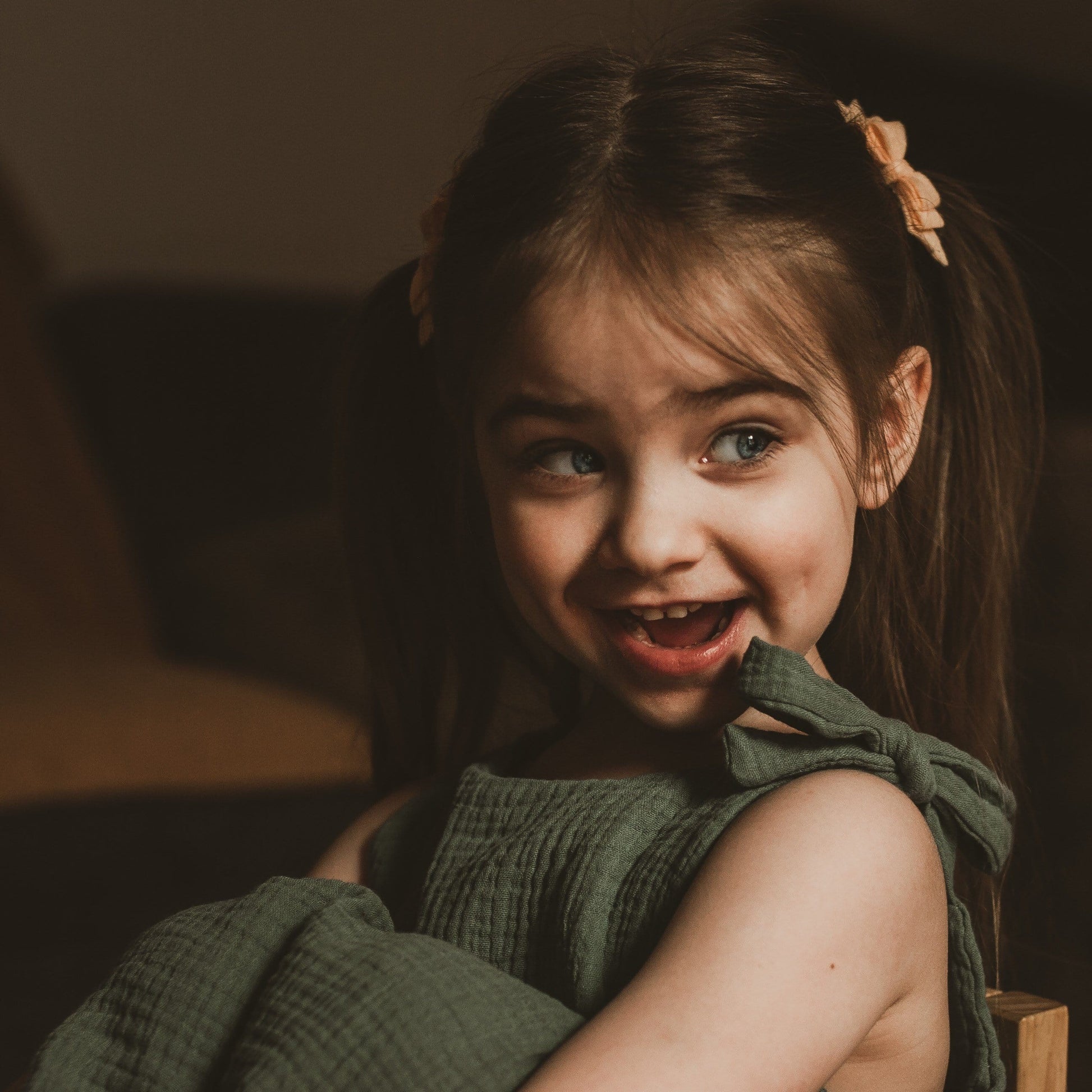 baby toddler girl sat smiling in her bedroom wearing a double gauze dress in forest green adjustable straps sustainable bohemian hippy beach clothing