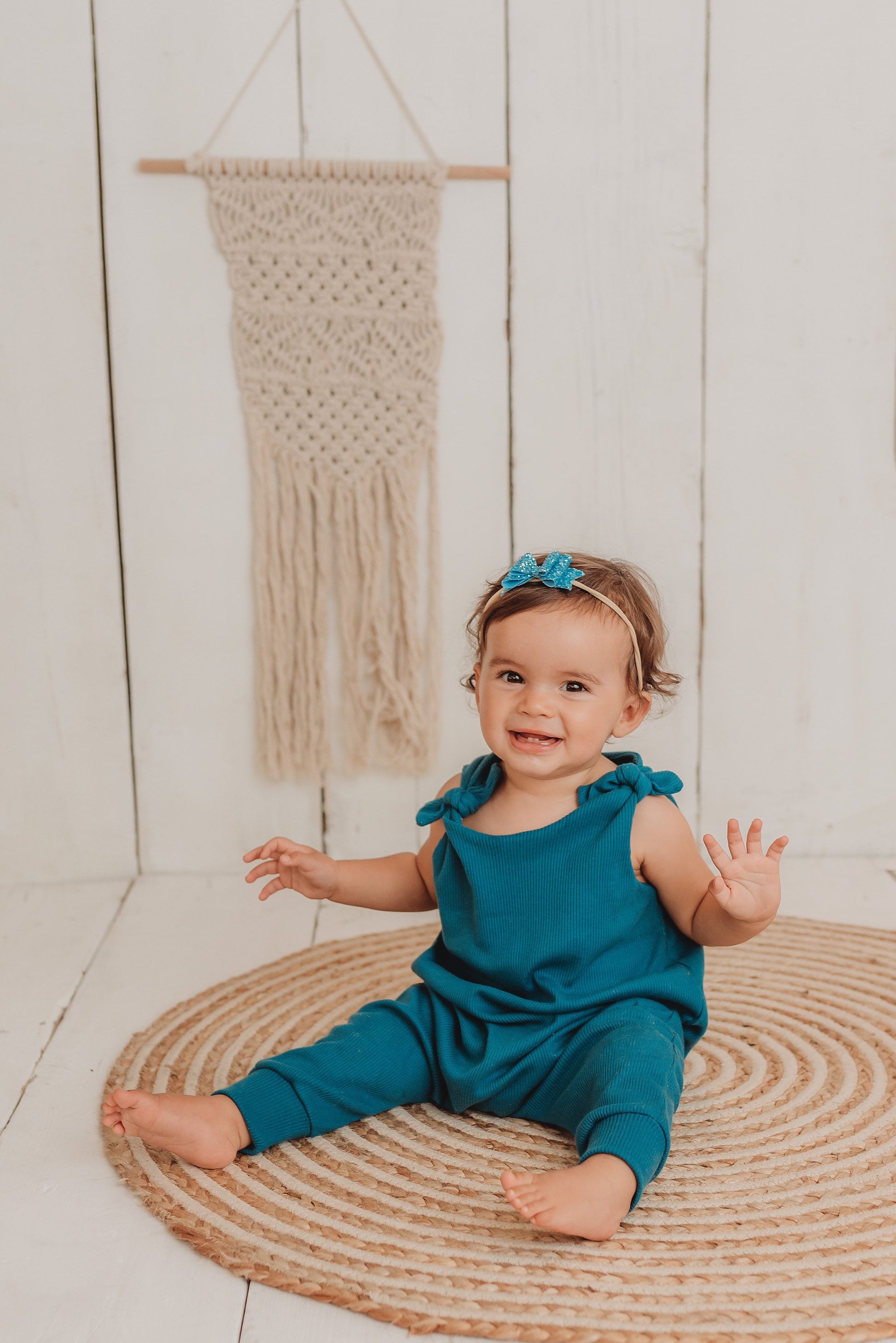 baby girl sits on the bohemian mat whilst wearing her handmade teal blue lounge comfy romper adjustable straps cosy winter clothing