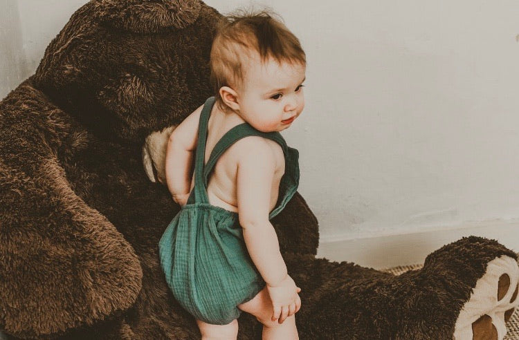 girl playing with teddy bear wearing the unisex forest green bohemian handmade summer romper with adjustable straps easy to layer up hippy sustainable baby toddler clothing 