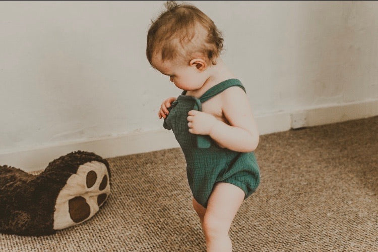 girl walking into a room wearing the forest green bohemian handmade summer romper with adjustable straps easy to layer up hippy sustainable baby toddler clothing 