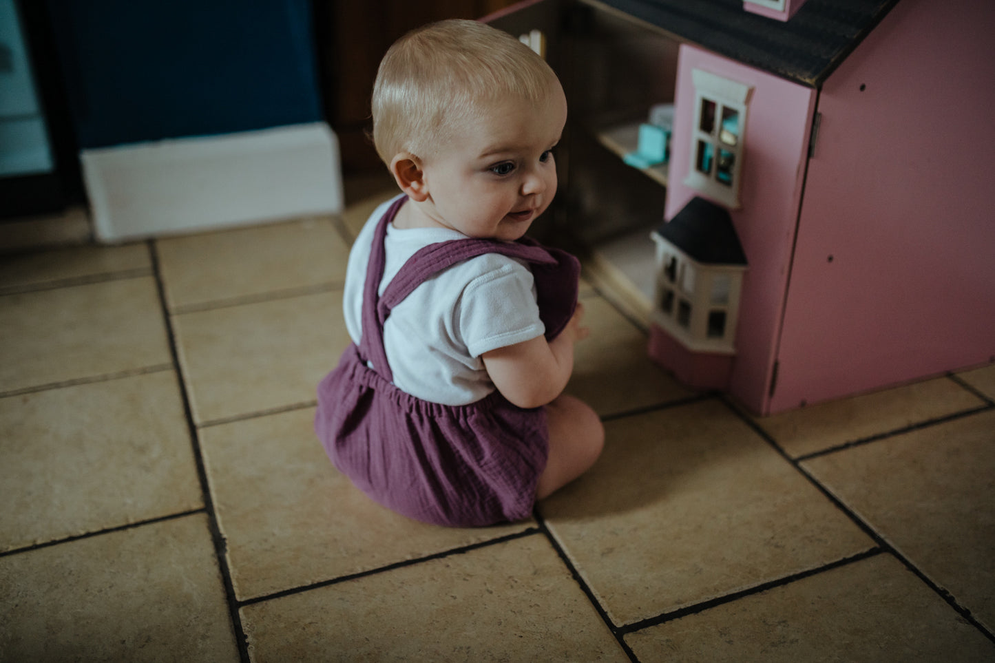 girl playing with dolls house wearing the purple bohemian handmade summer romper with adjustable straps easy to layer up hippy sustainable baby toddler clothing unisex